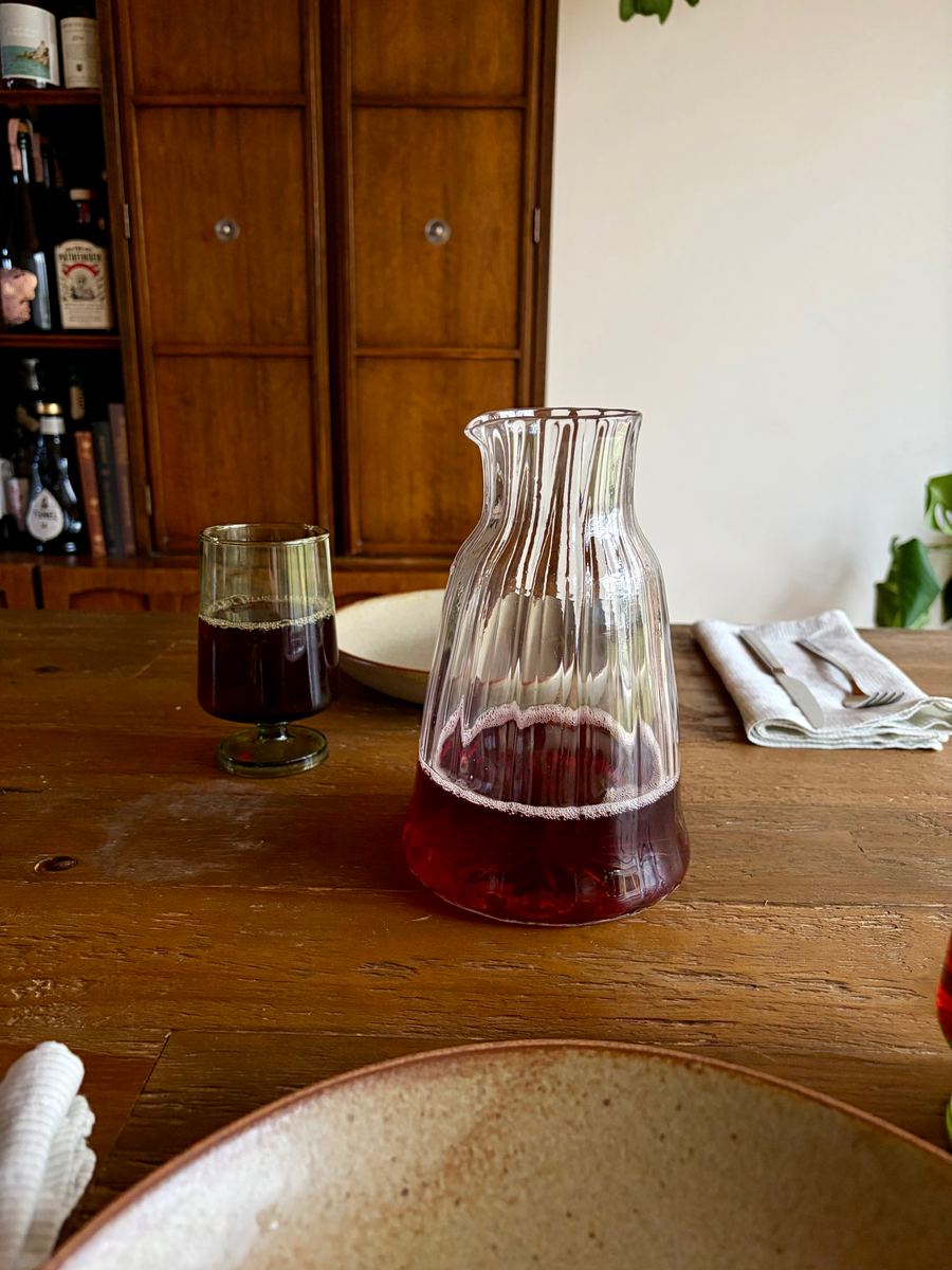 The decanter full of red wine next to a glass at the dinner table