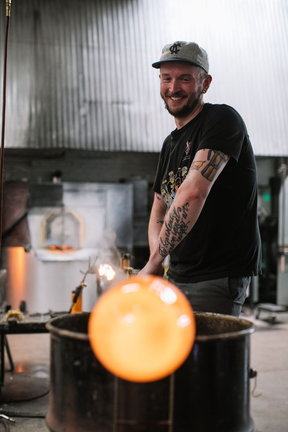 Austin Stern smiling over a glowing gather of glass in his studio